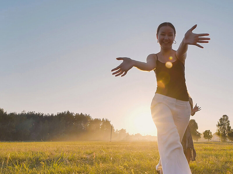 Young woman running joyfully across a meadow at sunrise