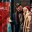 A couple standing at a shop window with a red poster with the words sale